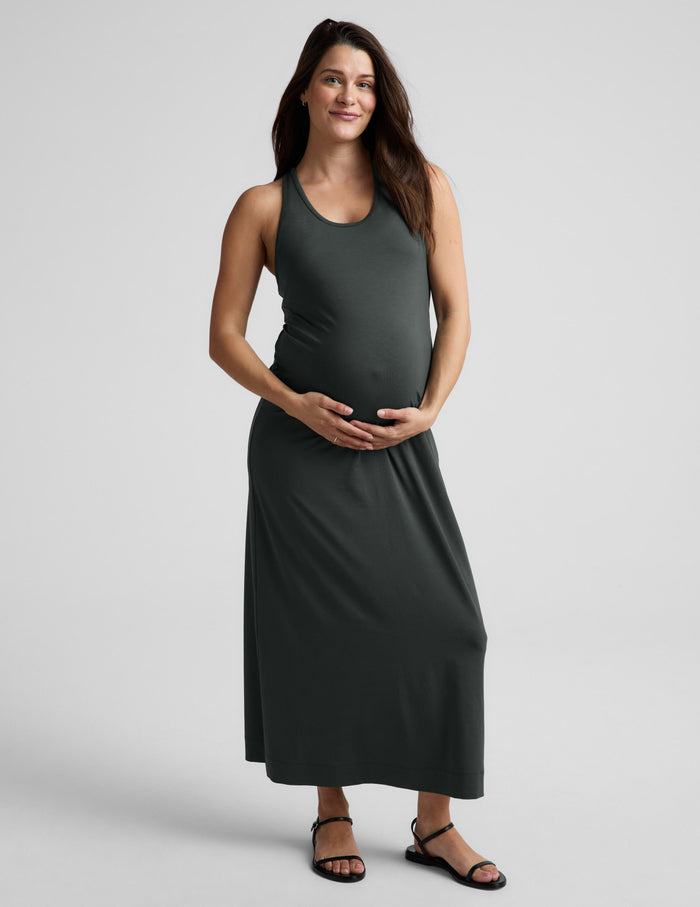 Woman wearing a dark green sleeveless dress on a light gray background.