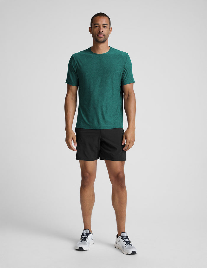 Man wearing a green t-shirt and black shorts on a light gray background.