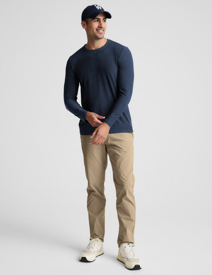 Man wearing a navy long sleeve shirt and khaki pants against a plain background.