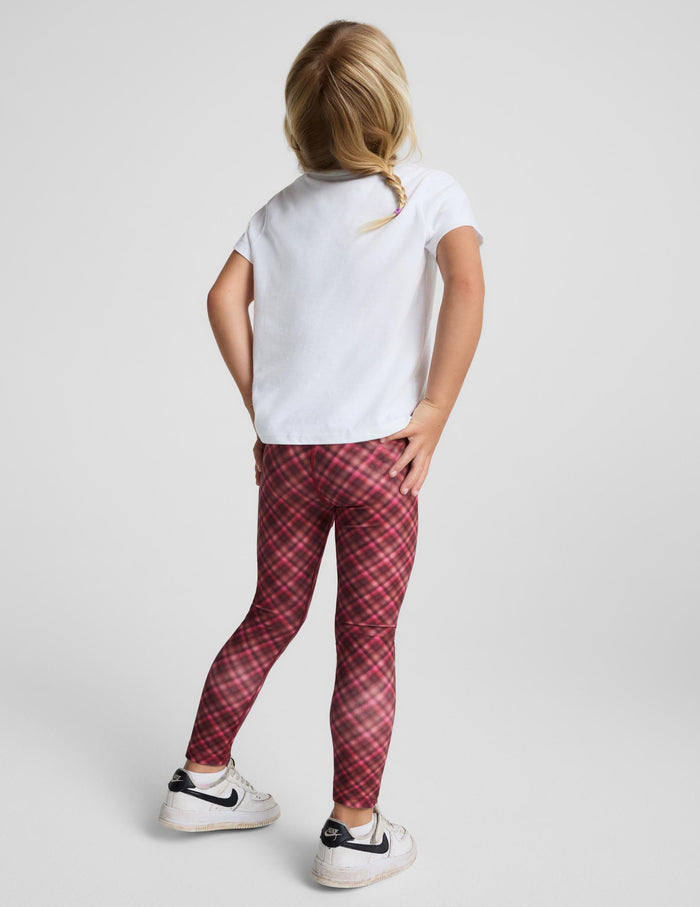 A child model shown from the back wearing red and black plaid leggings, a white t-shirt, and white sneakers with black accents, set against a plain light gray studio background.