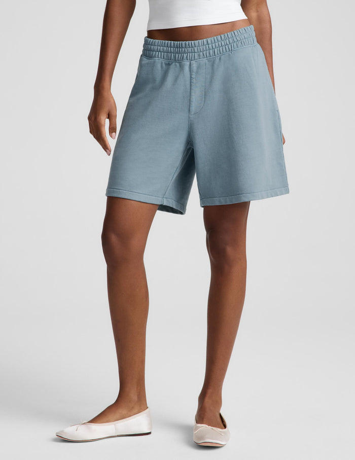 A woman modeling a white halter tank top and light blue bermuda shorts against a light gray studio background.