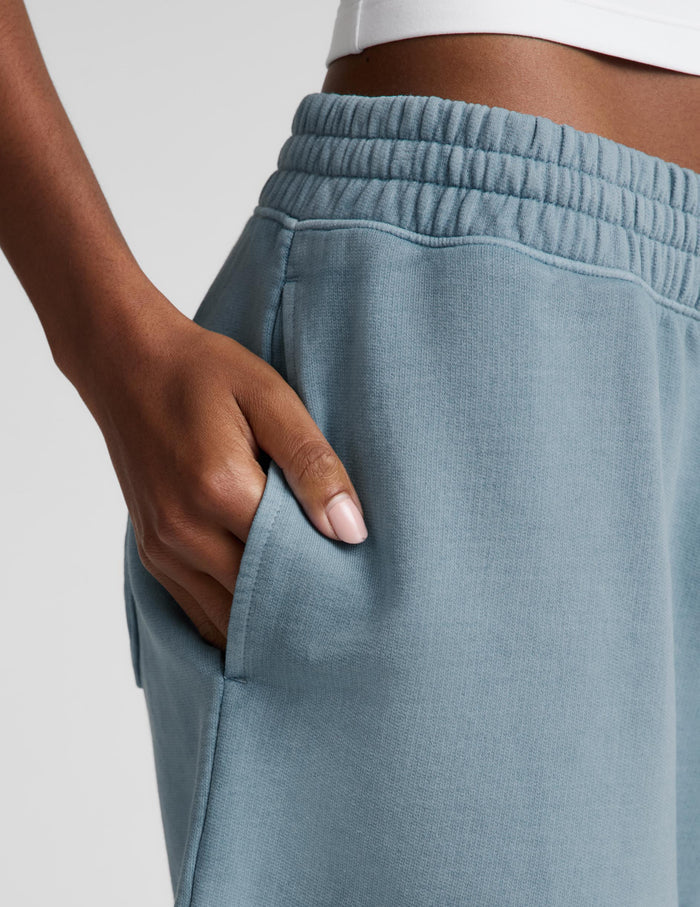 A woman modeling a white halter tank top and light blue bermuda shorts against a light gray studio background.