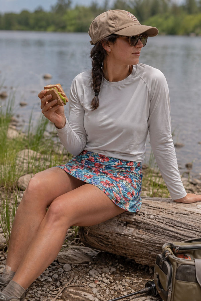 Woman sitting on a log by a lake, eating a sandwich