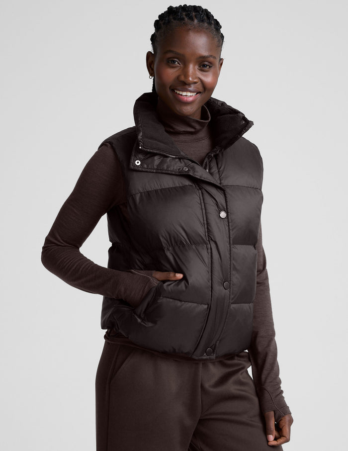person wearing a brown puffer vest and brown long sleeve top against a plain background.