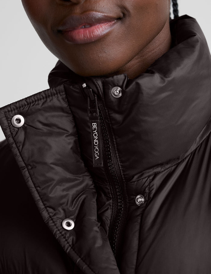 person wearing a brown puffer vest and brown long sleeve top against a plain background.
