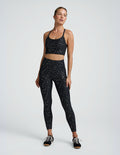 Woman wearing a black cropped tank with a mini moons print and leggings on a plain background.