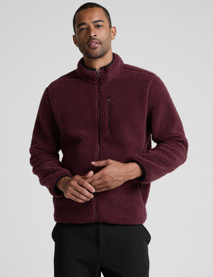 model wearing a burgundy fleece men's zip-up jacket on a gray background.