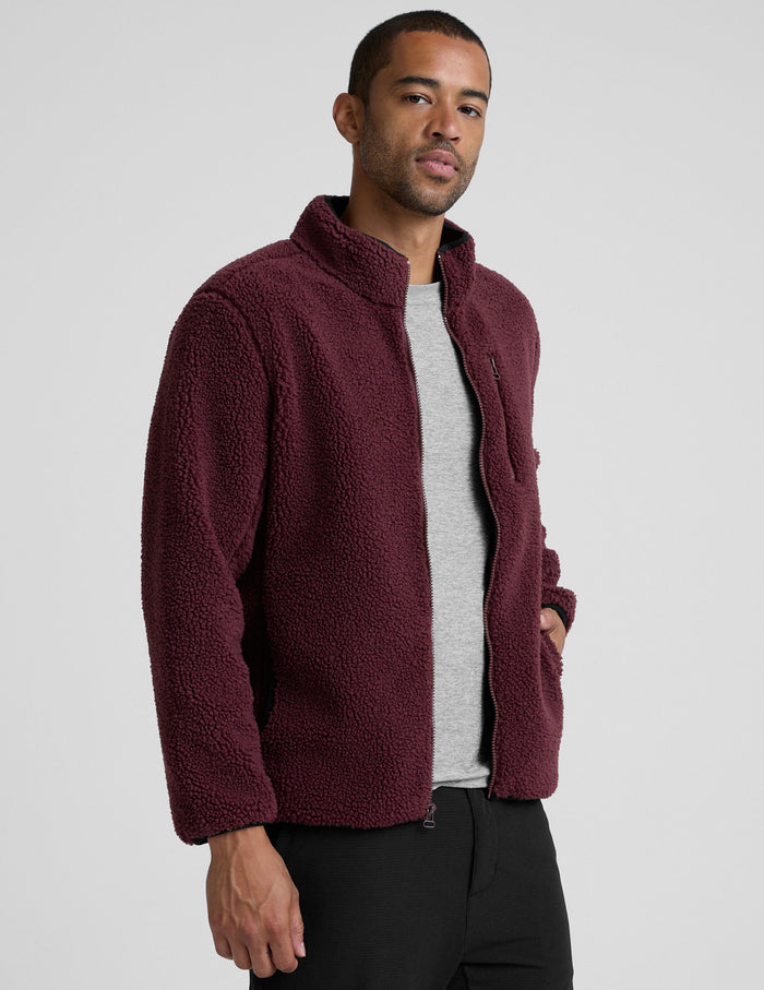 model wearing a burgundy fleece men's zip-up jacket on a gray background.