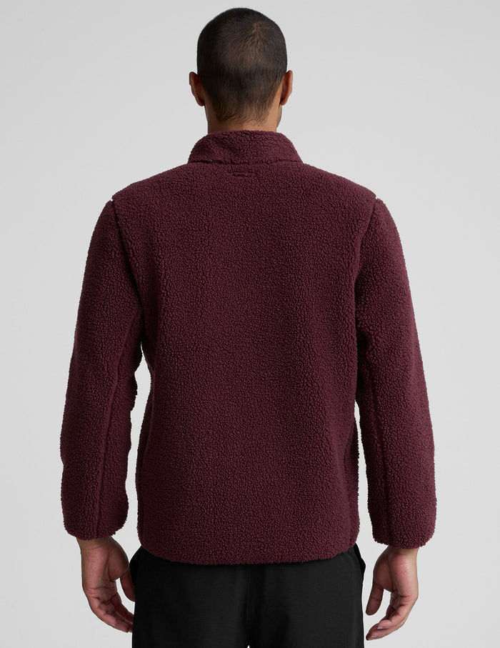model wearing a burgundy fleece men's zip-up jacket on a gray background.