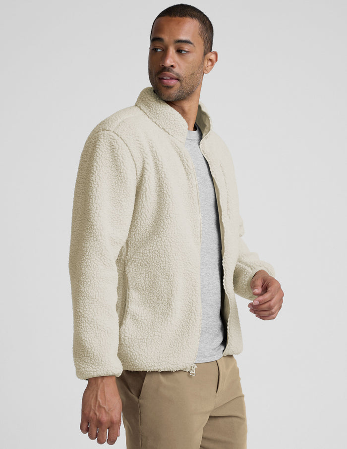model wearing a men's beige fleece zip-up jacket on a plain background.