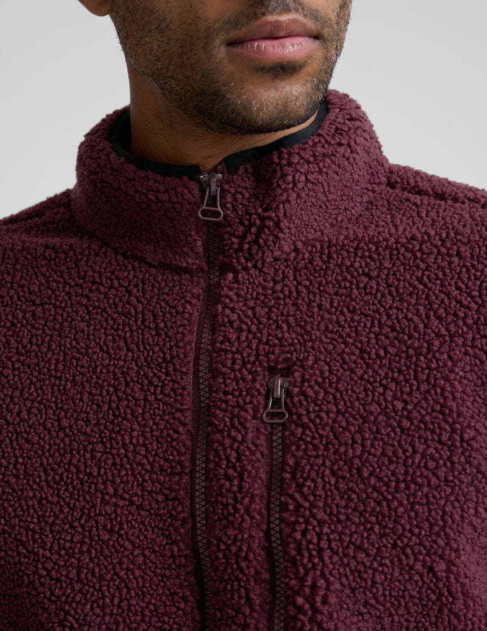 model wearing a burgundy fleece men's zip-up jacket on a gray background.