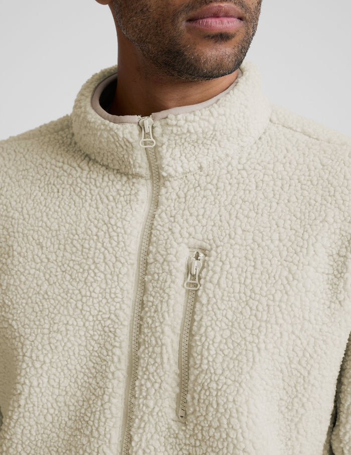 model wearing a men's beige fleece zip-up jacket on a plain background.