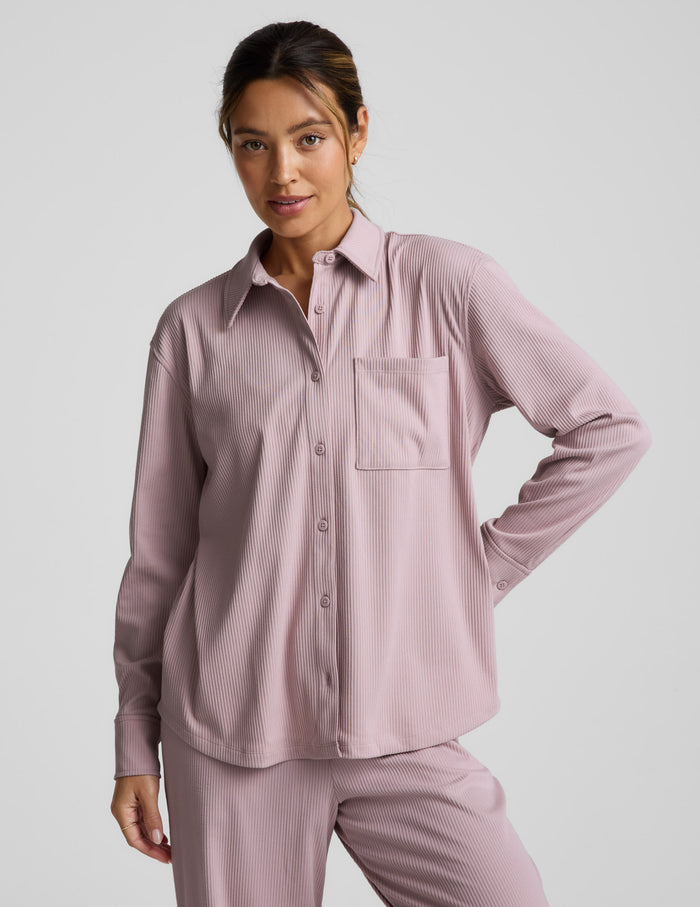 Woman wearing a pink corduroy button down shirt and pants against a plain background.