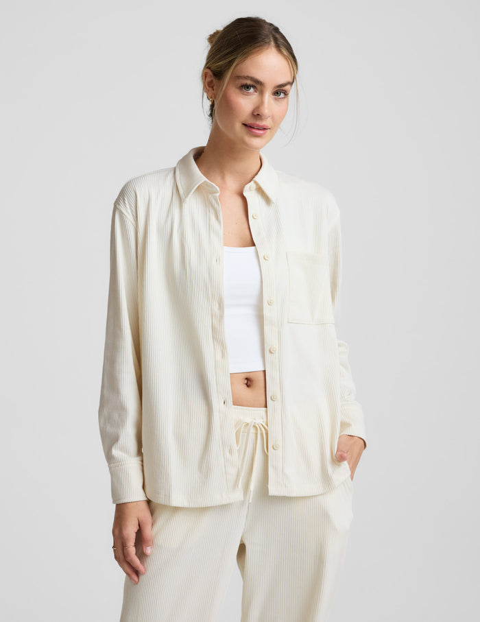 Woman wearing a cream-colored corduroy button up shirt and pants on a plain background.