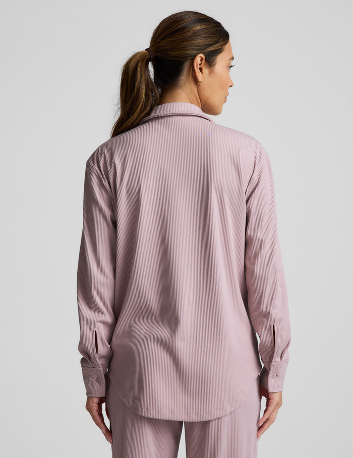 Woman wearing a pink corduroy button down shirt and pants against a plain background.