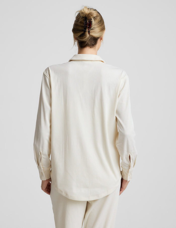 Woman wearing a cream-colored corduroy button up shirt and pants on a plain background.