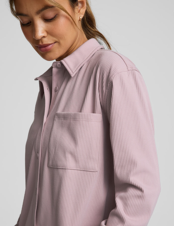 Woman wearing a pink corduroy button down shirt and pants against a plain background.