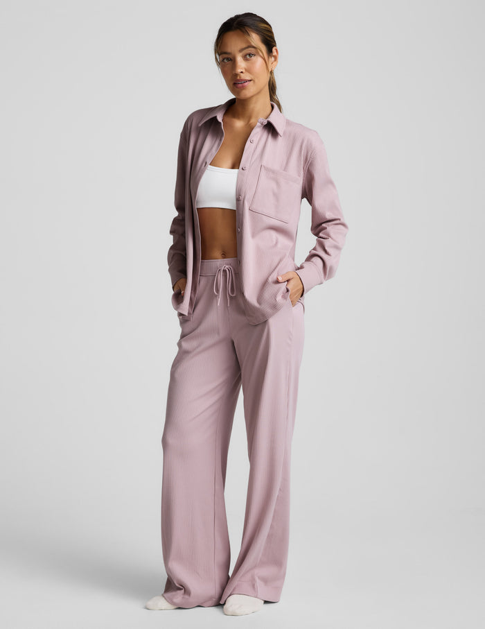 Woman wearing a pink corduroy button down shirt and pants against a plain background.