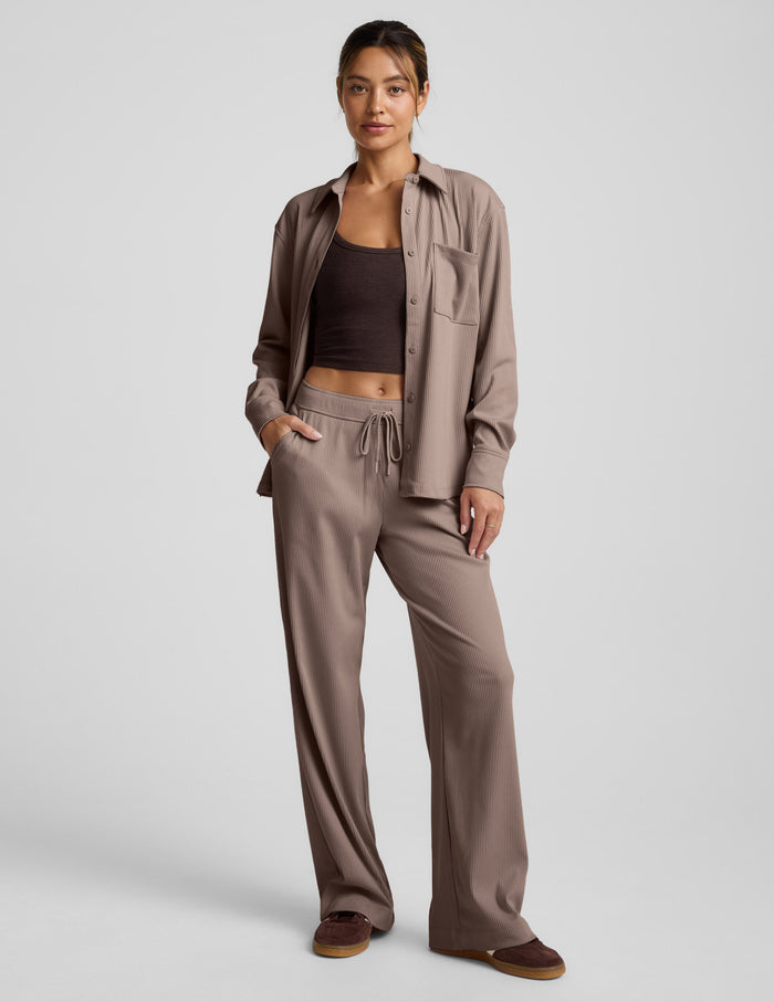 Woman wearing brown wide-leg corduroy pants and a button down top on a light gray background.