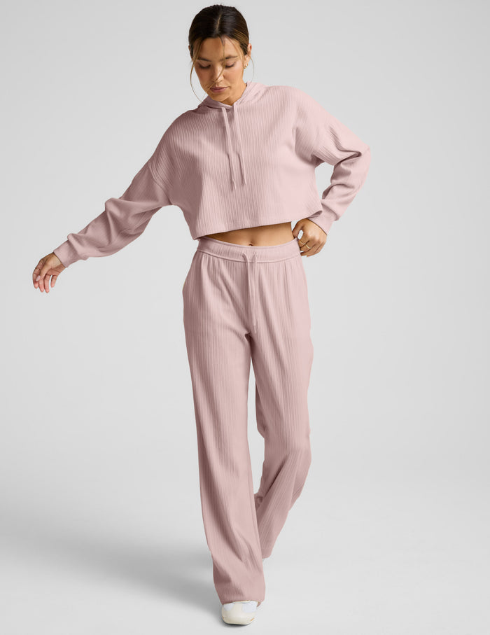 Woman wearing a ribbed cropped hoodie and pants on a plain background.
