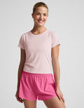 Woman wearing a light pink active short sleeve top and pink running shorts against a plain background.