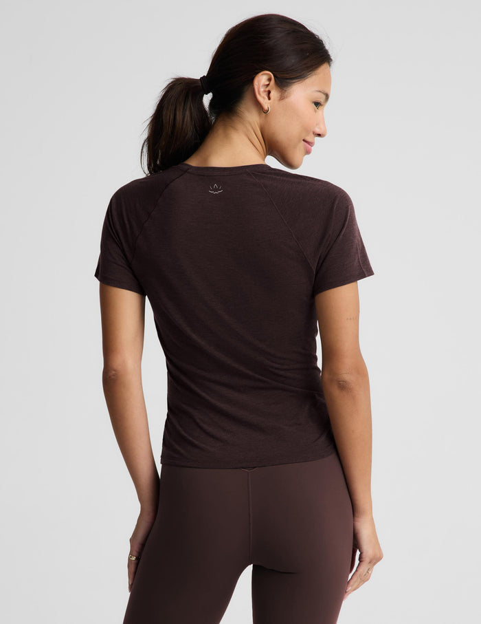 A woman shown from the back wearing a fitted short-sleeve athletic top and matching leggings in a dark brown color, against a light gray studio background.