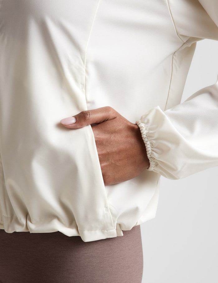 Close-up of a person wearing a cream-colored jacket with a hand in the pocket.