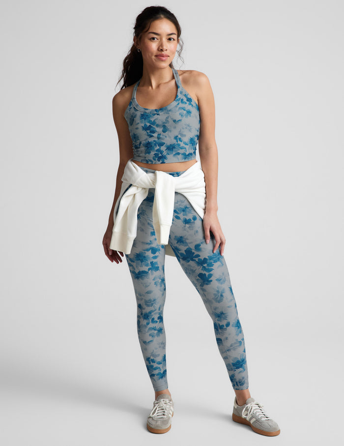 Woman wearing a blue floral sports bra and leggings on a light gray background.
