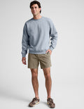 Saturday Men's Short in Olive green, featuring an elastic waist and mid-thigh length, worn by a model with a sweatshirt.