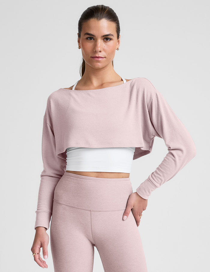 woman wearing a pink long-sleeve crop shrug and leggings on a plain background.