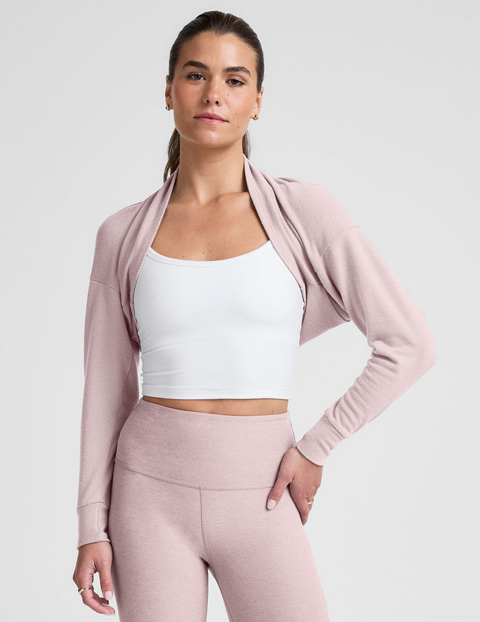 woman wearing a pink long-sleeve crop shrug and leggings on a plain background.