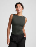 Woman wearing a green sleeveless top and black pants on a light gray background.