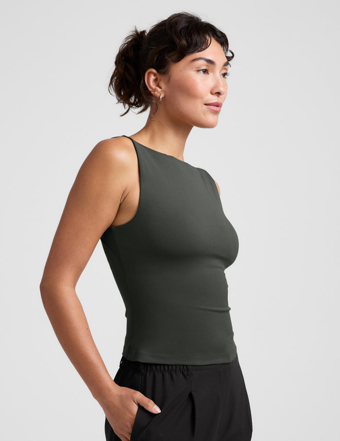 Woman wearing a green sleeveless top and black pants on a light gray background.