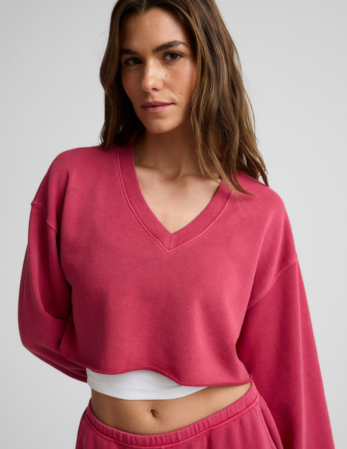 Woman wearing a red cropped long sleeve v-neck sweatshirt and shorts against a plain background.