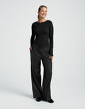 Smiling woman standing in black wide-leg Faux Leather Pant with drawstring elastic waistband and side pockets.