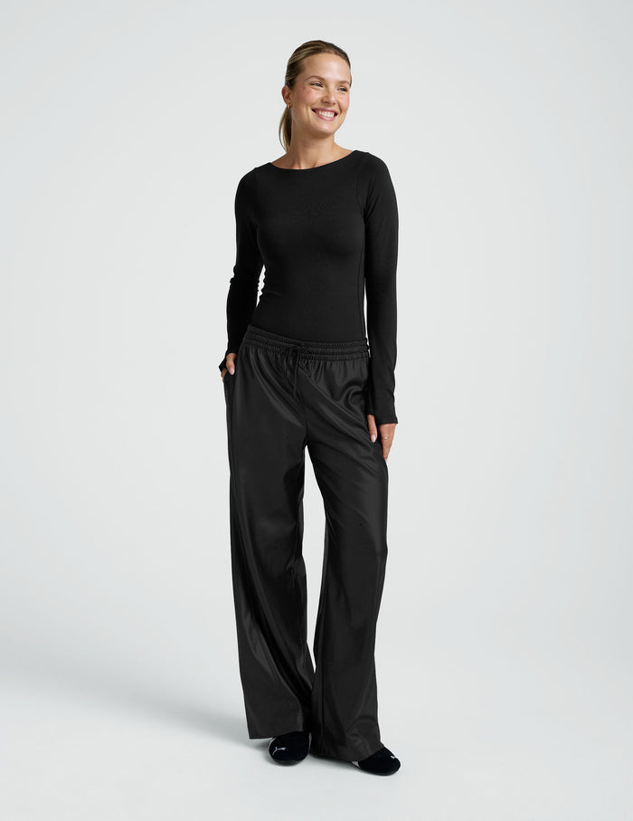 Smiling woman standing in black wide-leg Faux Leather Pant with drawstring elastic waistband and side pockets.
