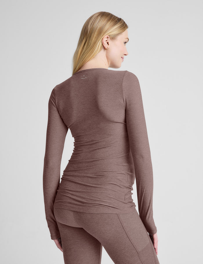 Woman wearing a brown maternity long-sleeve top and leggings against a light gray background.