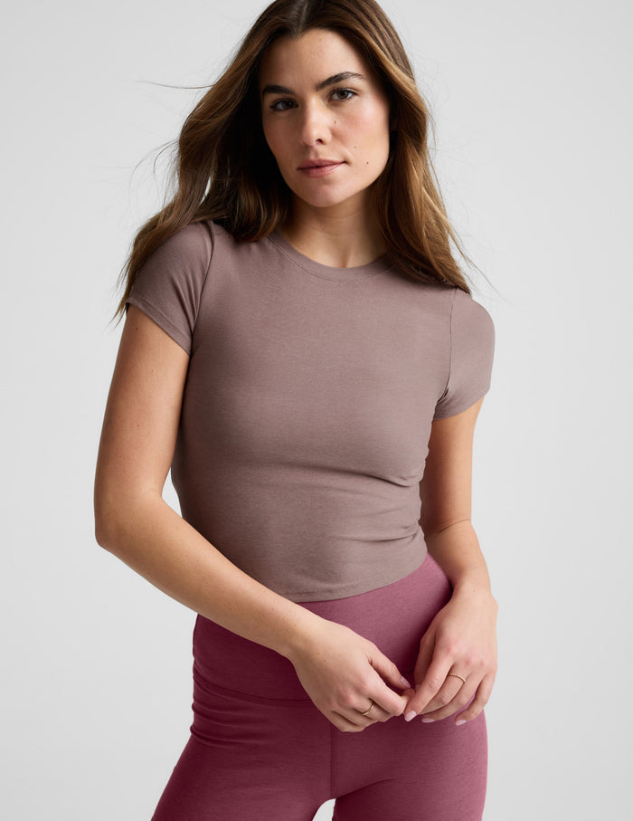 Woman wearing a brown cropped t-shirt and pink leggings against a plain background.