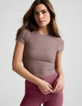 Woman wearing a brown cropped t-shirt and pink leggings against a plain background.