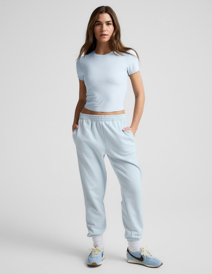 Woman wearing a blue cropped t-shirt and blue sweatpants against a plain background.