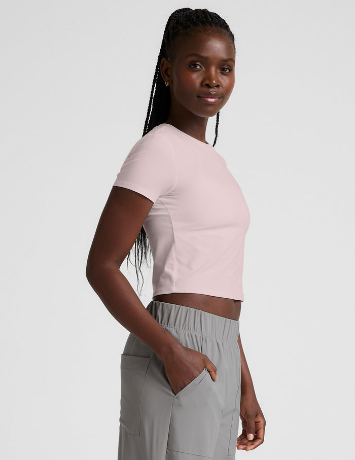 woman wearing a light pink crop top and gray pants on a white background.