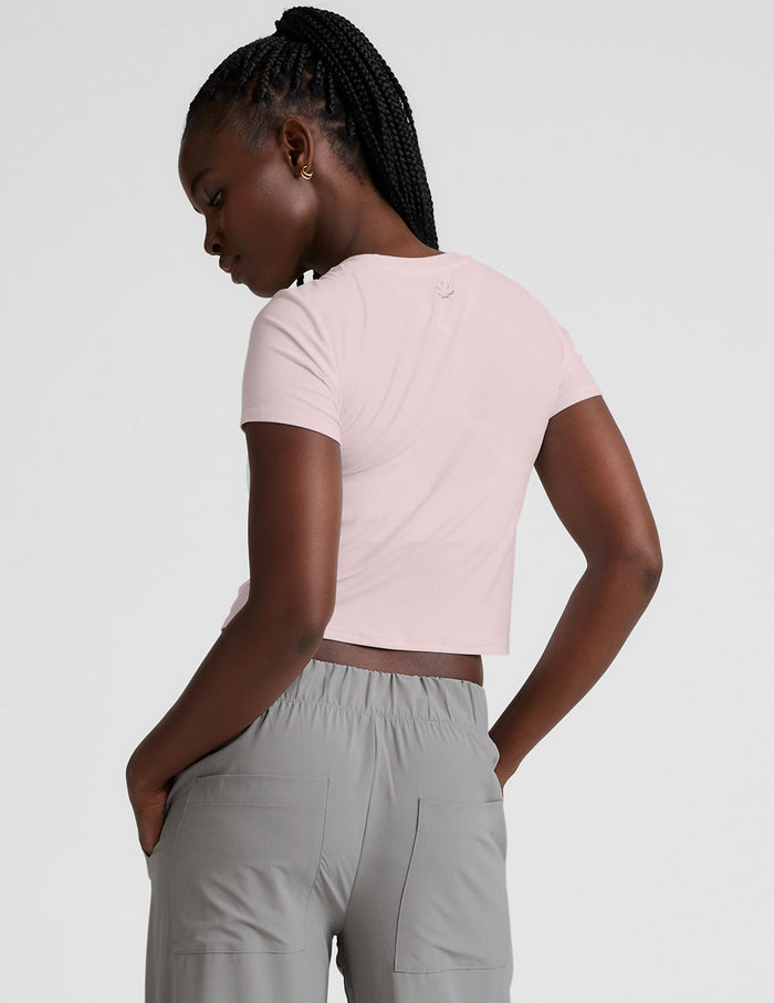 woman wearing a light pink crop top and gray pants on a white background.