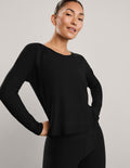 A woman modeling a black long-sleeve crewneck top and black biker shorts against a plain light gray studio background.