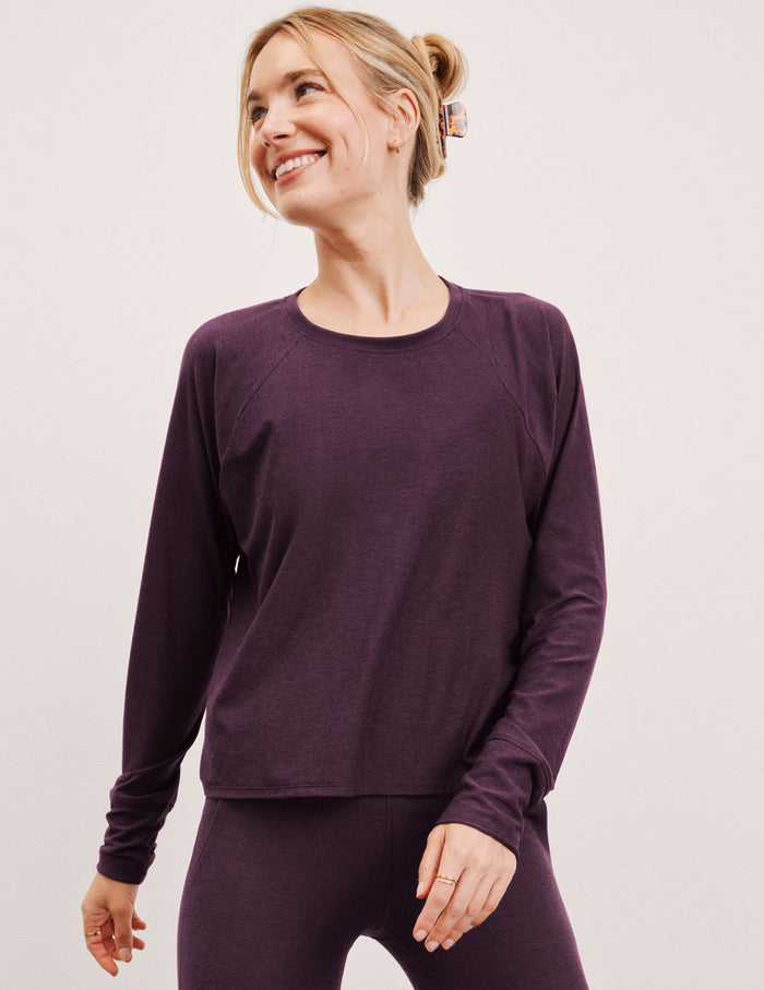 model wearing a purple scoop neck long-sleeve top and leggings on a light gray background.