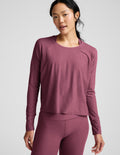 Woman wearing a purple long sleeve top and leggings against a light grey background.