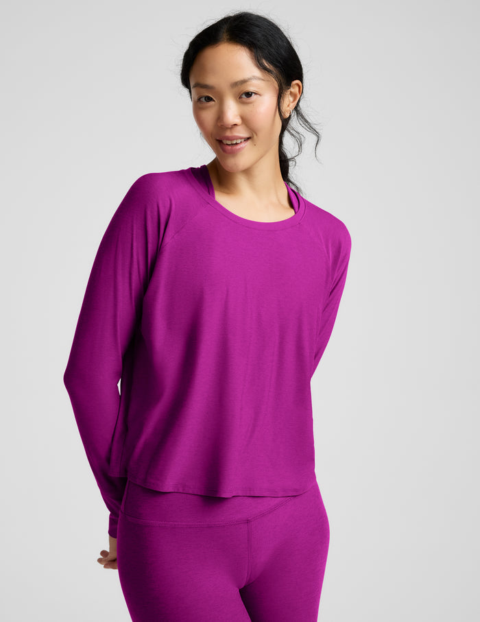 A woman modeling a matching magenta-purple long-sleeve top and leggings set against a solid light gray background.