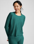Woman wearing a teal long-sleeve top and leggings on a light gray background.