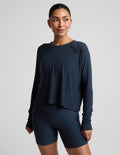 A woman modeling a dark navy blue long-sleeve crop top and matching high-waisted bike shorts against a light gray studio background.