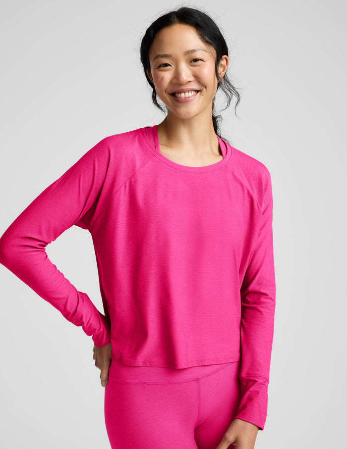 Woman wearing a bright pink long-sleeve top and leggings on a light gray background.