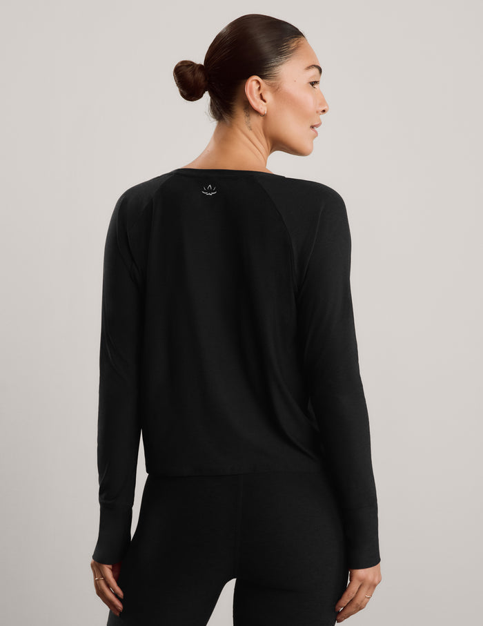 A woman modeling a black long-sleeve crewneck top and black biker shorts against a plain light gray studio background.